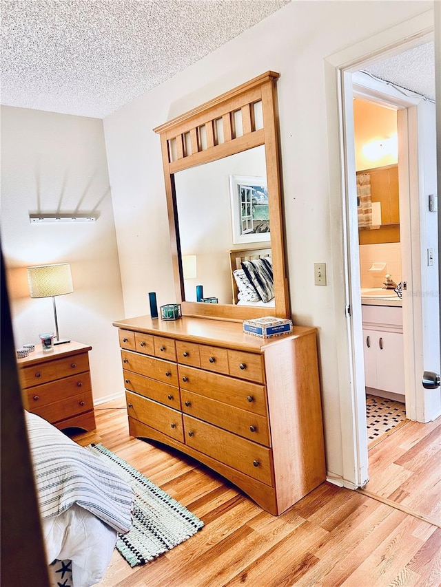 bedroom with ensuite bathroom, a textured ceiling, and light hardwood / wood-style flooring