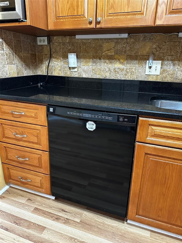 kitchen with black dishwasher, light hardwood / wood-style flooring, dark stone countertops, and backsplash