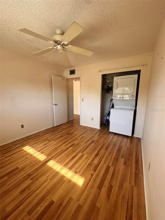 unfurnished bedroom featuring a textured ceiling, ceiling fan, stacked washer and clothes dryer, and hardwood / wood-style flooring