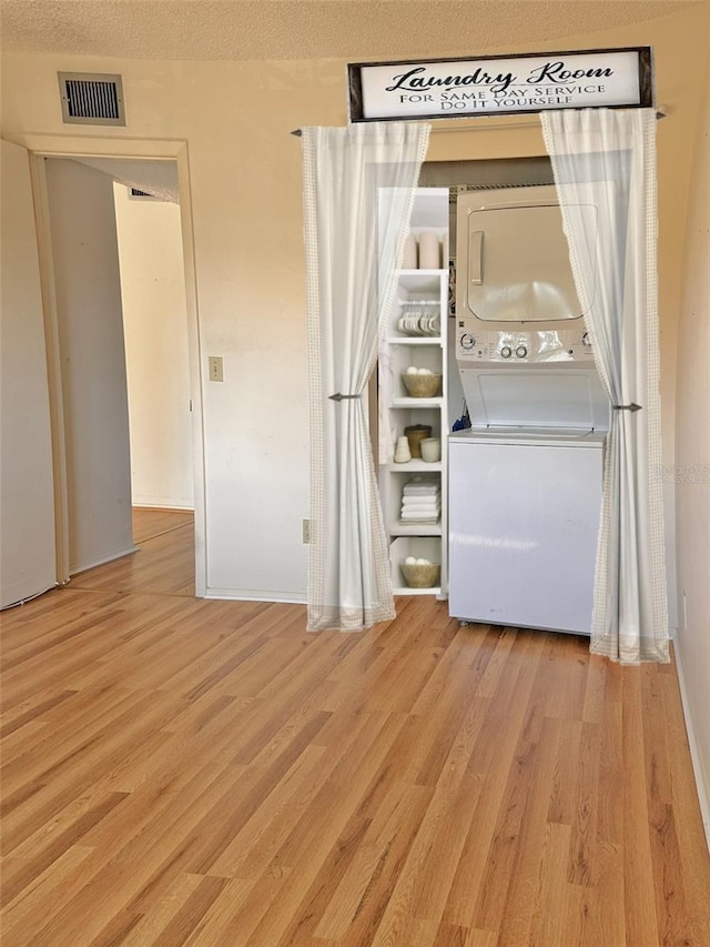 laundry area with a textured ceiling, light wood-type flooring, and stacked washer and dryer