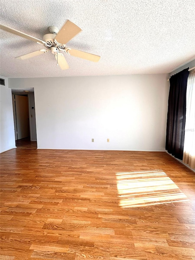 empty room with ceiling fan, a textured ceiling, and light wood-type flooring