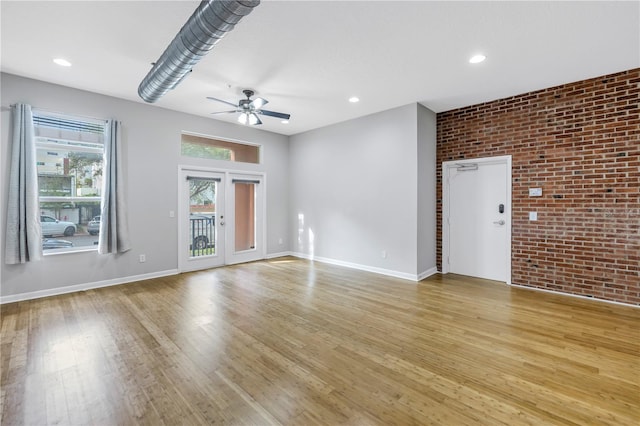 unfurnished room with brick wall, ceiling fan, light wood-type flooring, and french doors