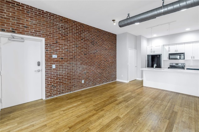 interior space with brick wall, light hardwood / wood-style flooring, white cabinetry, and black appliances