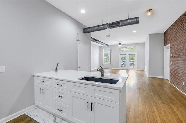 kitchen featuring brick wall, ceiling fan, white cabinetry, and sink