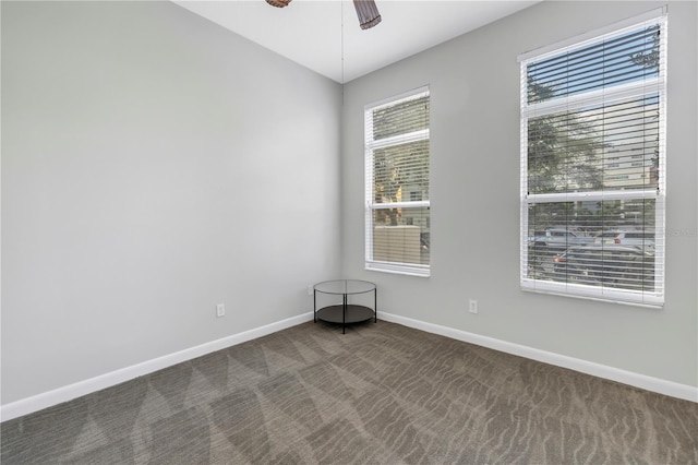 unfurnished room with plenty of natural light, dark carpet, and ceiling fan