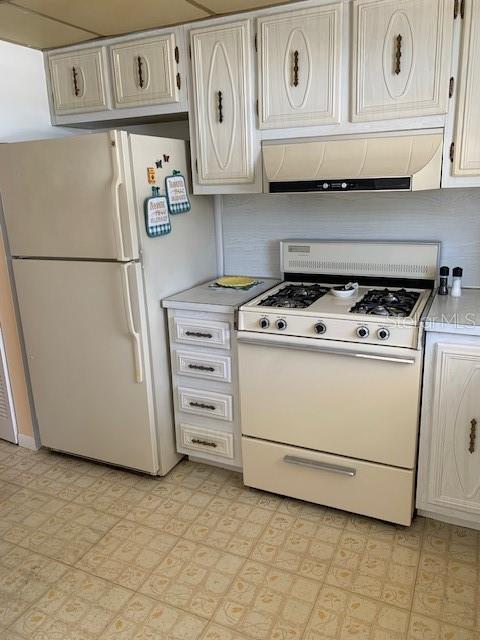 kitchen with white appliances, white cabinets, custom range hood, and light tile floors