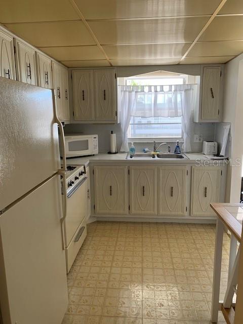 kitchen featuring light tile flooring, white appliances, a drop ceiling, and sink