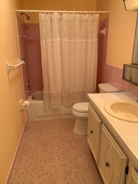 full bathroom with tile floors, large vanity, shower / bath combo with shower curtain, and toilet