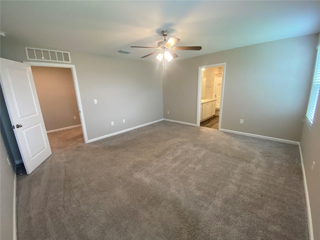 unfurnished bedroom with ceiling fan, ensuite bathroom, and dark carpet