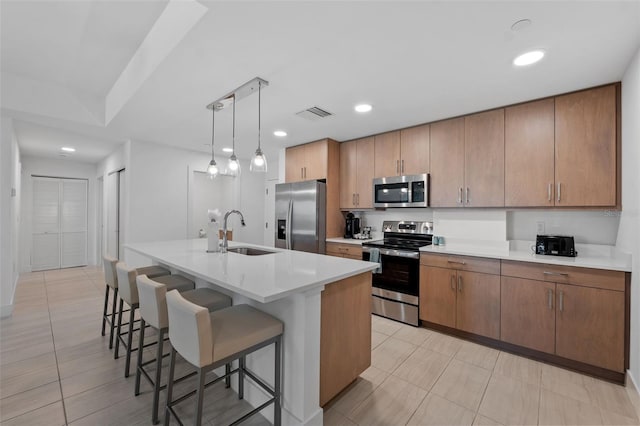 kitchen featuring stainless steel appliances, pendant lighting, light tile patterned floors, a center island with sink, and sink