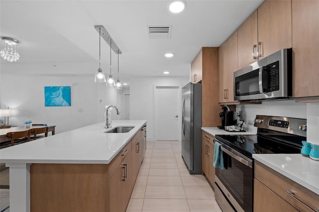 kitchen featuring stainless steel appliances, light tile patterned floors, pendant lighting, a center island with sink, and sink