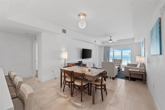 tiled dining area with ceiling fan and a raised ceiling