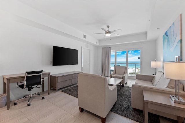 tiled living room featuring ceiling fan and a tray ceiling