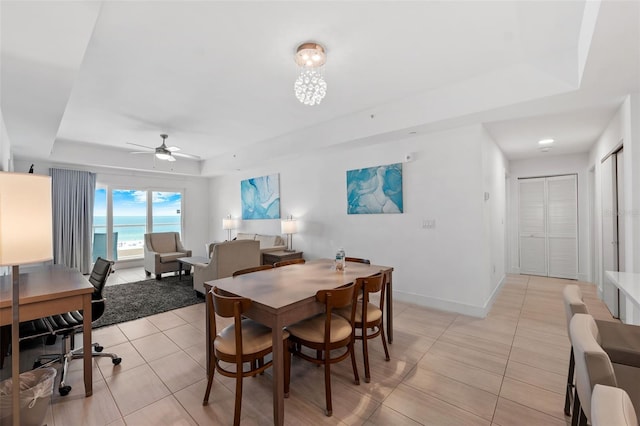 dining area with ceiling fan, a water view, a raised ceiling, and light tile patterned floors