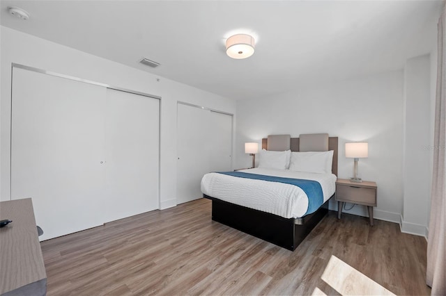 bedroom with multiple closets and light wood-type flooring