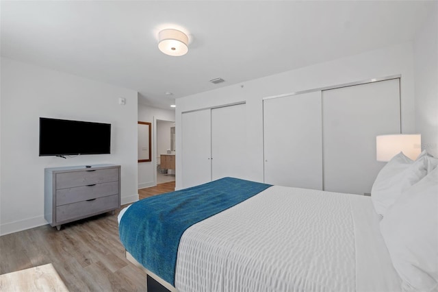 bedroom with two closets, light hardwood / wood-style flooring, and connected bathroom