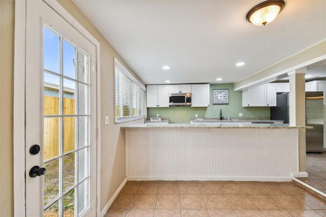 kitchen featuring appliances with stainless steel finishes, kitchen peninsula, white cabinetry, and light stone countertops