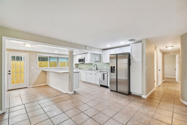 kitchen with appliances with stainless steel finishes, light tile patterned floors, kitchen peninsula, and white cabinetry