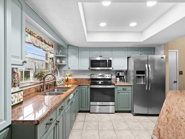 kitchen featuring light tile flooring, appliances with stainless steel finishes, a tray ceiling, and sink