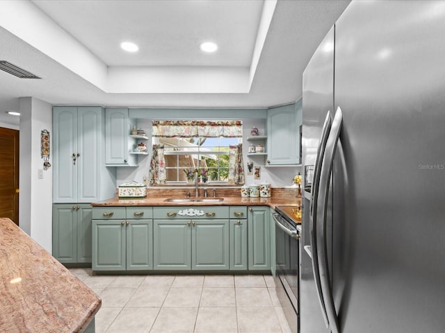 kitchen featuring a tray ceiling, stainless steel fridge, sink, light tile floors, and electric range oven