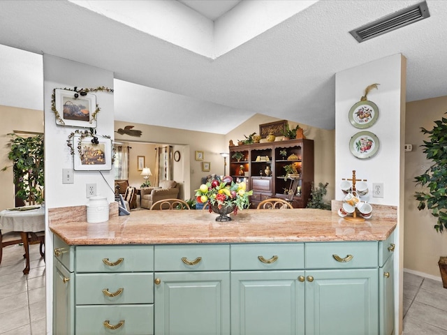 kitchen with light tile floors, kitchen peninsula, a textured ceiling, and light stone counters