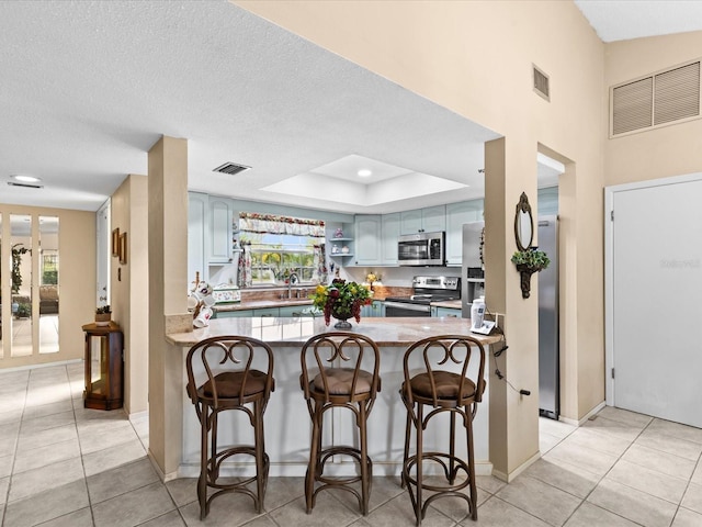 kitchen with light tile floors, appliances with stainless steel finishes, kitchen peninsula, and a breakfast bar area