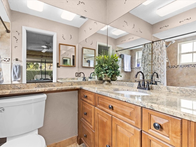 bathroom with dual sinks, toilet, ceiling fan, and vanity with extensive cabinet space