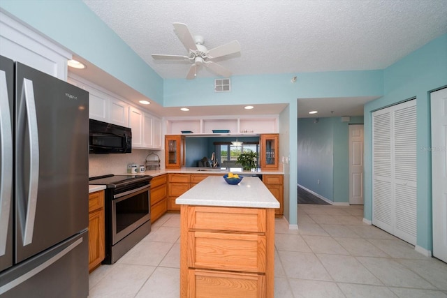 kitchen with light tile floors, appliances with stainless steel finishes, a center island, ceiling fan, and a textured ceiling