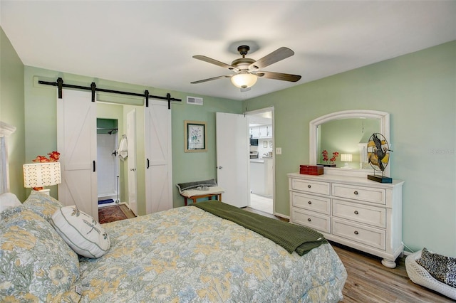 bedroom featuring dark wood-style floors, visible vents, a barn door, a ceiling fan, and baseboards