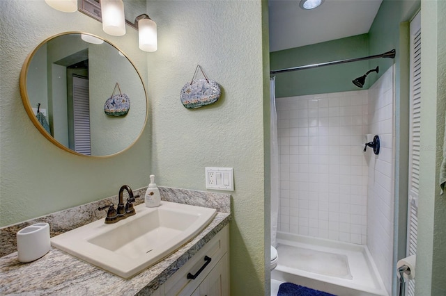 full bathroom with toilet, a textured wall, a shower stall, and vanity