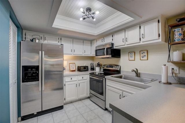 kitchen featuring a tray ceiling, appliances with stainless steel finishes, ornamental molding, white cabinetry, and a sink