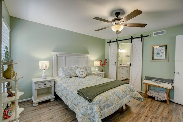 bedroom featuring visible vents, a barn door, a ceiling fan, wood finished floors, and baseboards