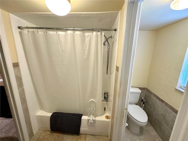 full bathroom featuring shower / bathtub combination with curtain, wainscoting, tile walls, toilet, and tile patterned floors