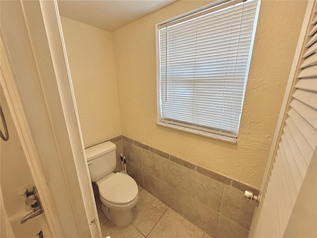 bathroom featuring tile patterned floors, a wainscoted wall, toilet, tile walls, and a textured wall