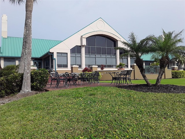 rear view of property with a standing seam roof, a patio area, a lawn, and metal roof