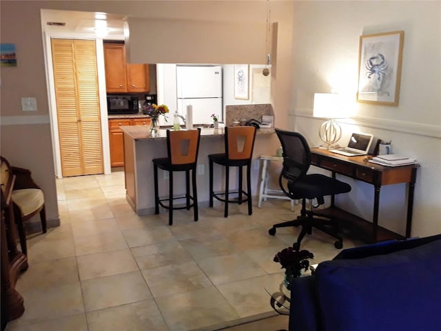 kitchen with a breakfast bar, freestanding refrigerator, a peninsula, brown cabinetry, and black microwave