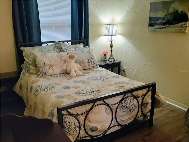 bedroom with wood finished floors, a textured wall, and baseboards