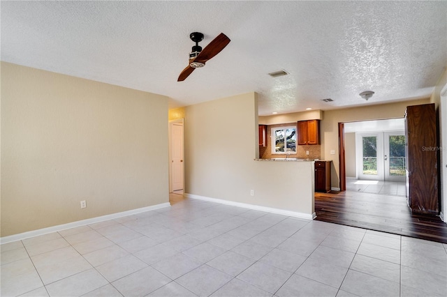 unfurnished living room with ceiling fan, a textured ceiling, light hardwood / wood-style flooring, and french doors