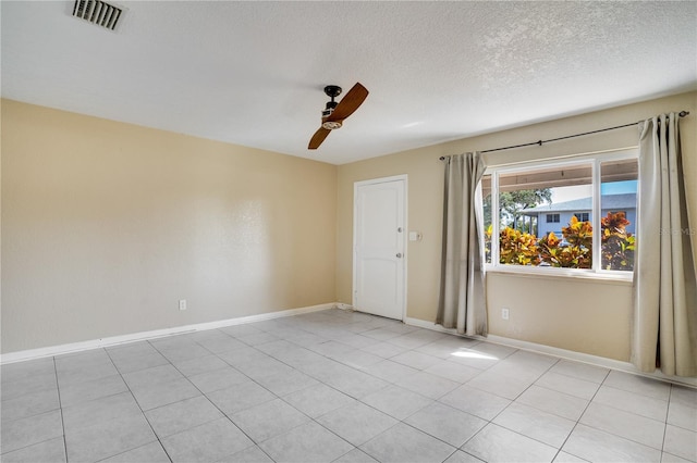 empty room featuring a textured ceiling, light tile patterned floors, and ceiling fan