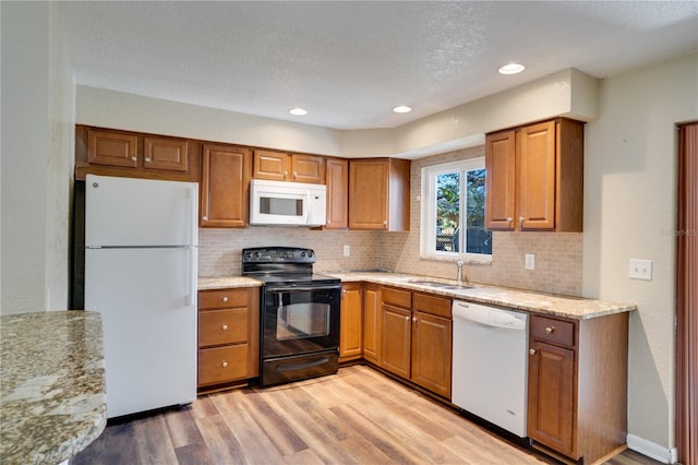 kitchen with sink, tasteful backsplash, a textured ceiling, white appliances, and light hardwood / wood-style flooring