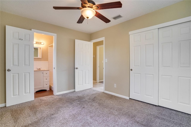 unfurnished bedroom featuring ensuite bathroom, ceiling fan, light carpet, and a closet