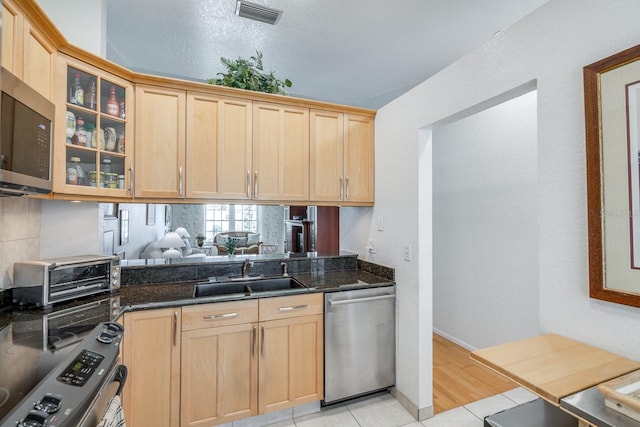 kitchen with stainless steel appliances, sink, dark stone countertops, and light tile patterned floors