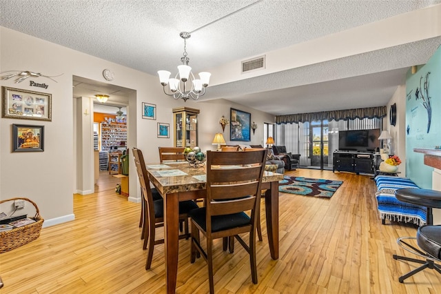 dining room with light hardwood / wood-style floors, a textured ceiling, and a notable chandelier