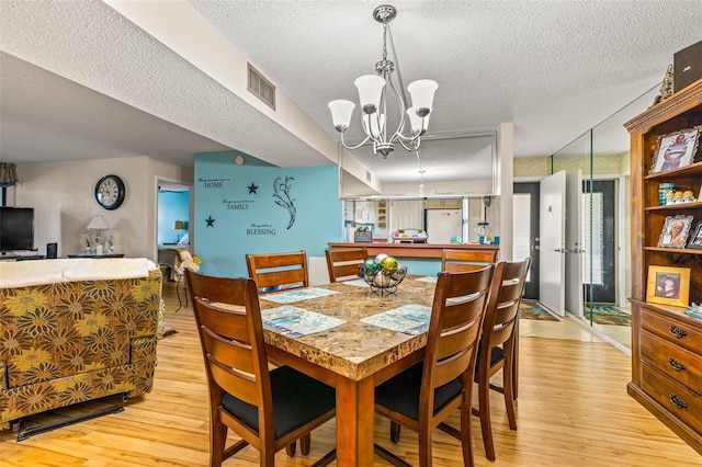 dining space with a notable chandelier, a textured ceiling, and light wood-type flooring