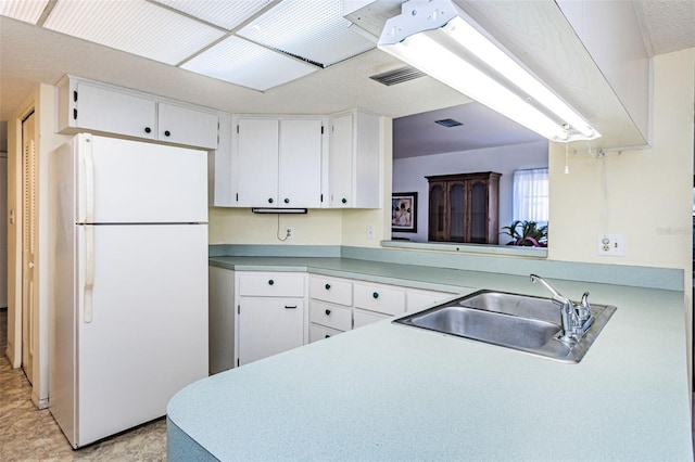 kitchen with light tile floors, white fridge, kitchen peninsula, white cabinets, and sink