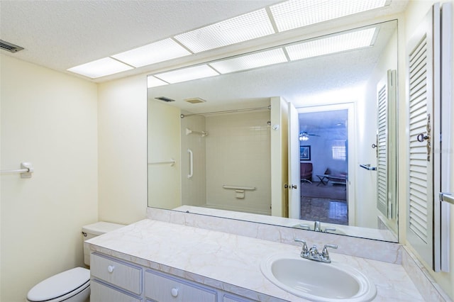 bathroom with a textured ceiling, oversized vanity, ceiling fan, and toilet