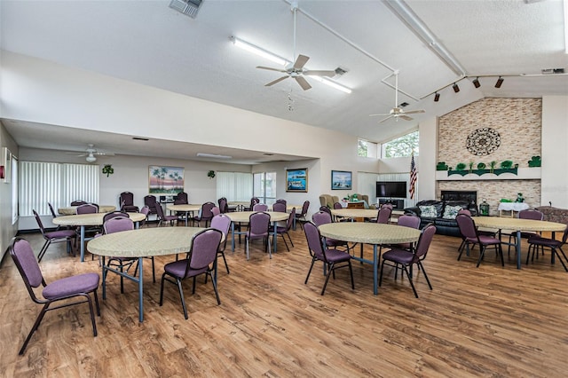 dining area with lofted ceiling, ceiling fan, a fireplace, light hardwood / wood-style floors, and a textured ceiling