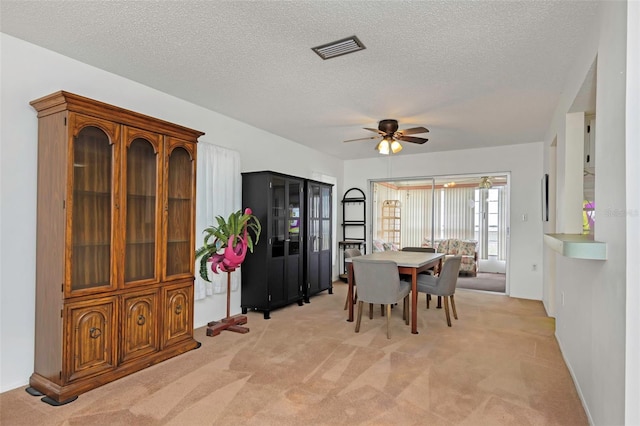 dining space with ceiling fan, light carpet, and a textured ceiling