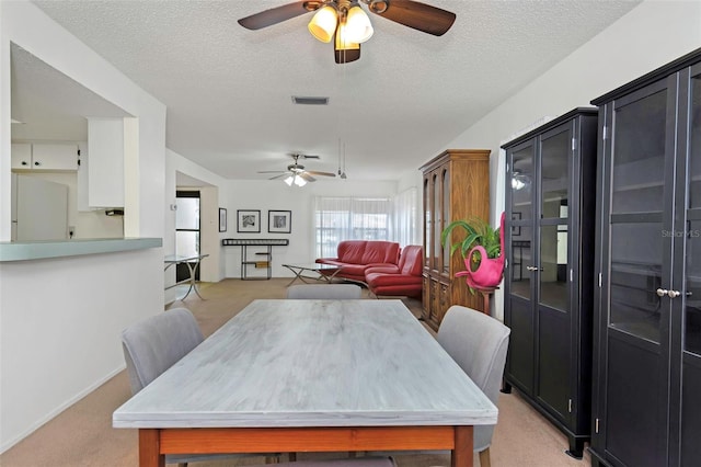 dining area with ceiling fan, light colored carpet, and a textured ceiling