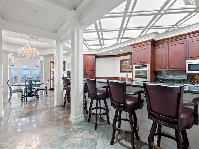 kitchen featuring oven, backsplash, decorative columns, an inviting chandelier, and pendant lighting